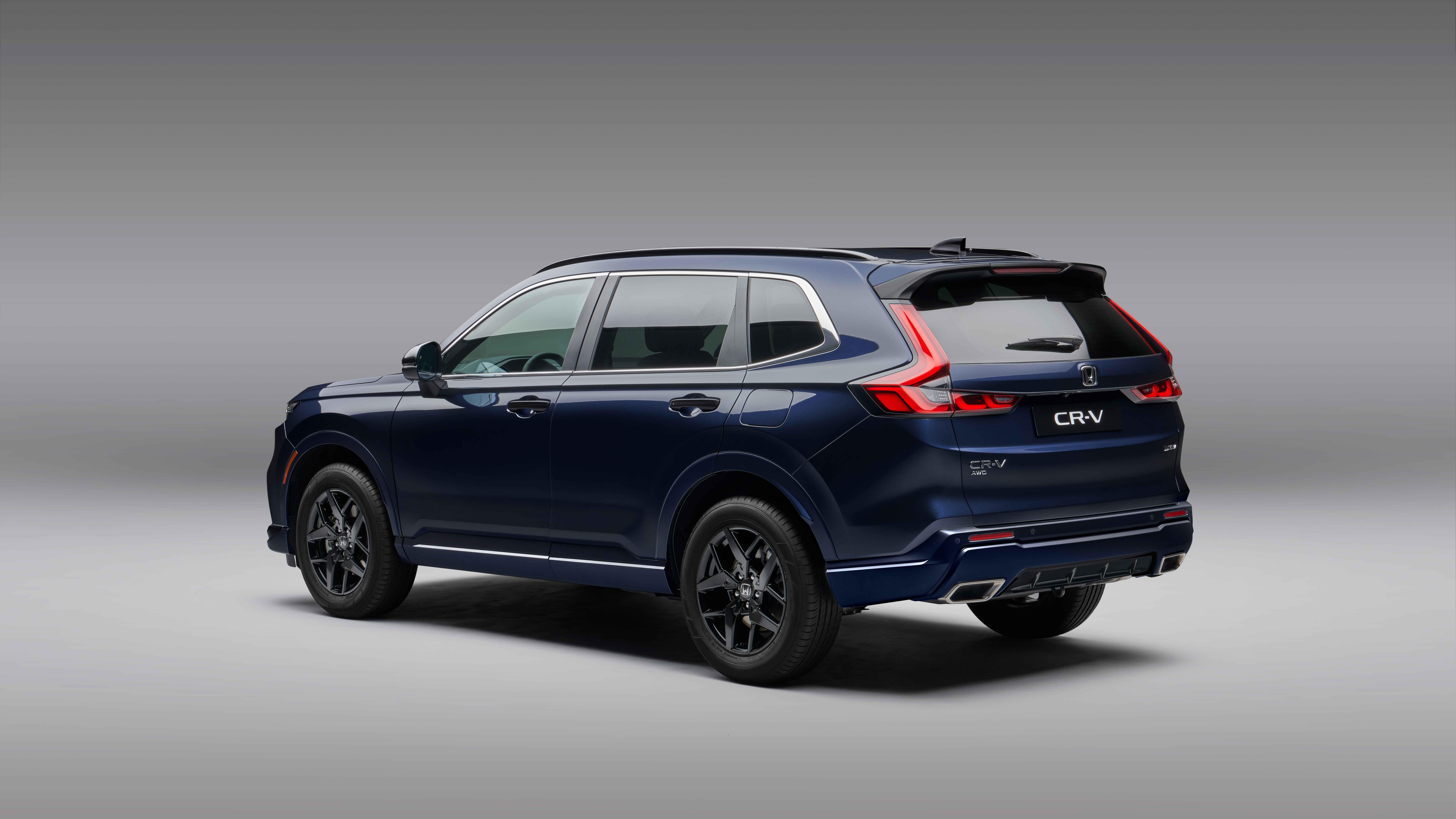 A dark blue Honda CR-V SUV, viewed from the rear three-quarter angle, showcasing its sleek design, alloy wheels, and distinctive taillights against a neutral gray background.